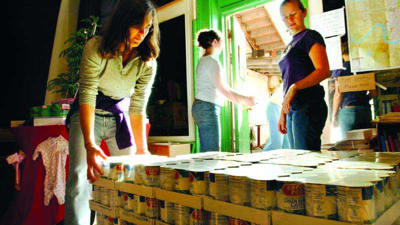 A group of people organize food pallets in a warehouse for distribution, maps of louisana on the wall in the background