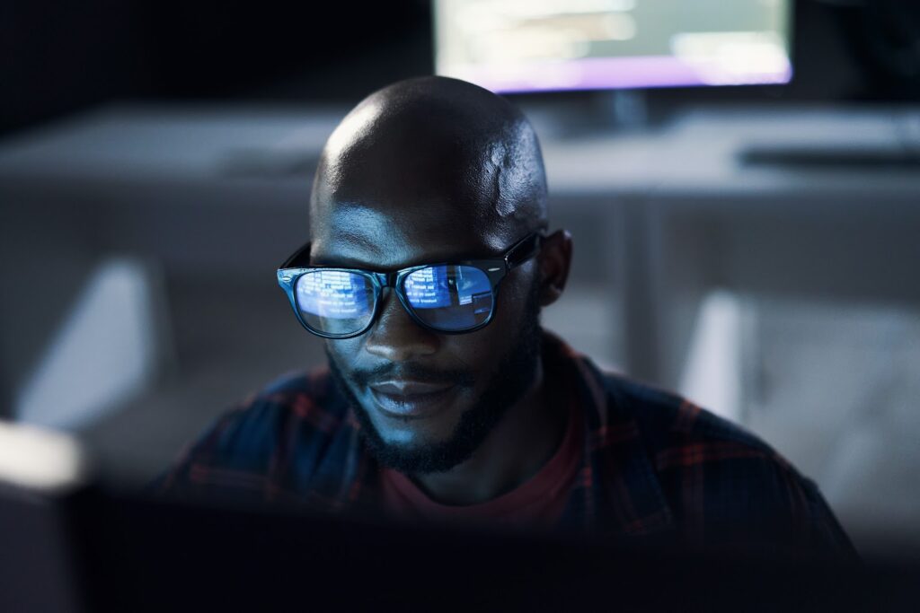 A Black male student wearing glasses works at a computer.