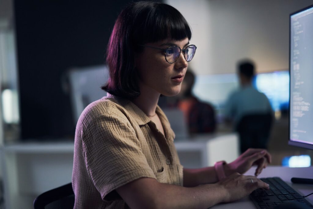 A woman wearing glasses works at a desktop computer.