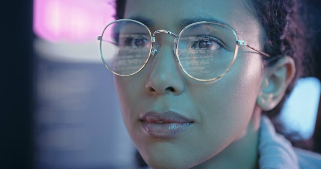 Close up of a computer scientist working at a computer screen; the coding script on her screen is reflected in her eyeglasses.